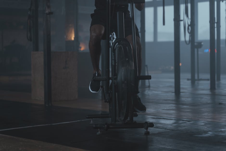 Close-up of legs cycling on stationary bike in gym showing quadriceps and calf muscles engaged during indoor cycling workout