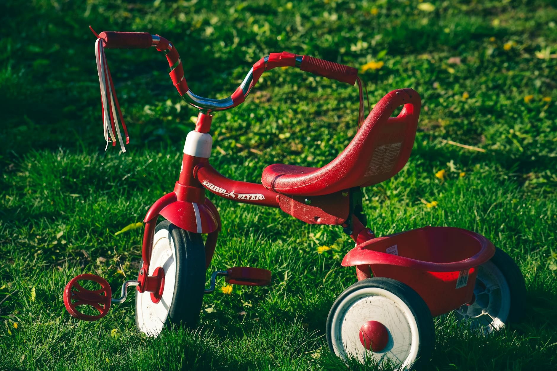 Vibrant red tricycle parked on a sunlit grassy lawn